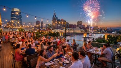 Nashville rooftop restaurant patio at dusk on the Fourth of July with diners, downtown skyline, Cumberland River and fireworks behind