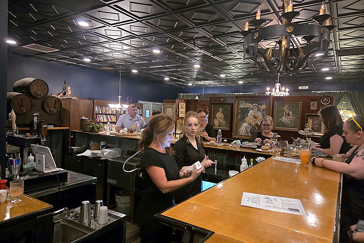 The bar at The Raven Book Lounge, backed by wine barrels and framed portraits