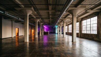 Interior of a converted early-1900s concrete warehouse with mushroom-capital columns, industrial windows and purple and teal accent lighting (illustrative)