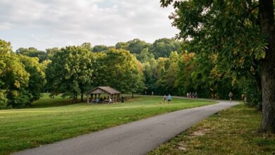 A Middle Tennessee city park on an early-September afternoon, with a paved greenway path, a wooden picnic shelter and green hardwoods just beginning to turn (illustrative)
