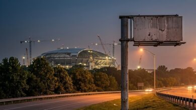 Empty roadside sign pole beside an interstate with a stadium under construction at dusk (illustrative)