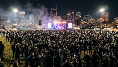 Crowd and lit concert stage in a city park on New Year's Eve with skyline behind (illustrative)